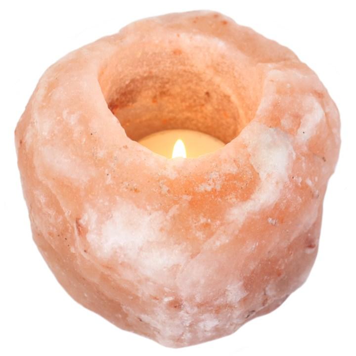 picure shows a rough hewn pink himalayan salt tealight holder, with a burning tealight on a white background. The pink himalayan salt tealight or candle holder is a rough round shape slightly bigger than a tennis ball