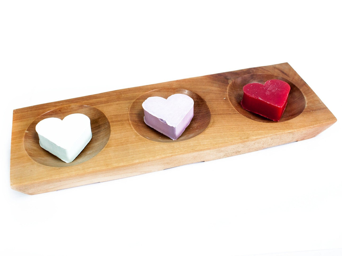 Wooden bath bomb holder on a white background. The bath bomb holder has three heart shaped  small soaps in it, one soap in slightly dipped bay which is there to hold the bath bombs or soaps. The soaps in the wooden bath bomb holder from left to right are white, light pink and red,